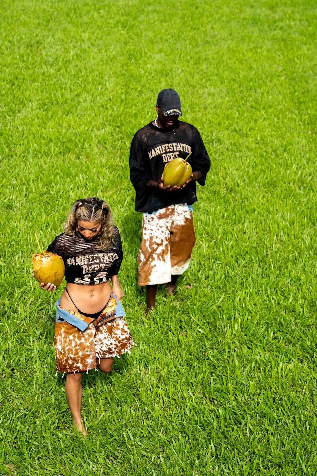 Overhead view of two models in black 42 jerseys and brown cowhide shorts holding yellow balls in a bright green field.