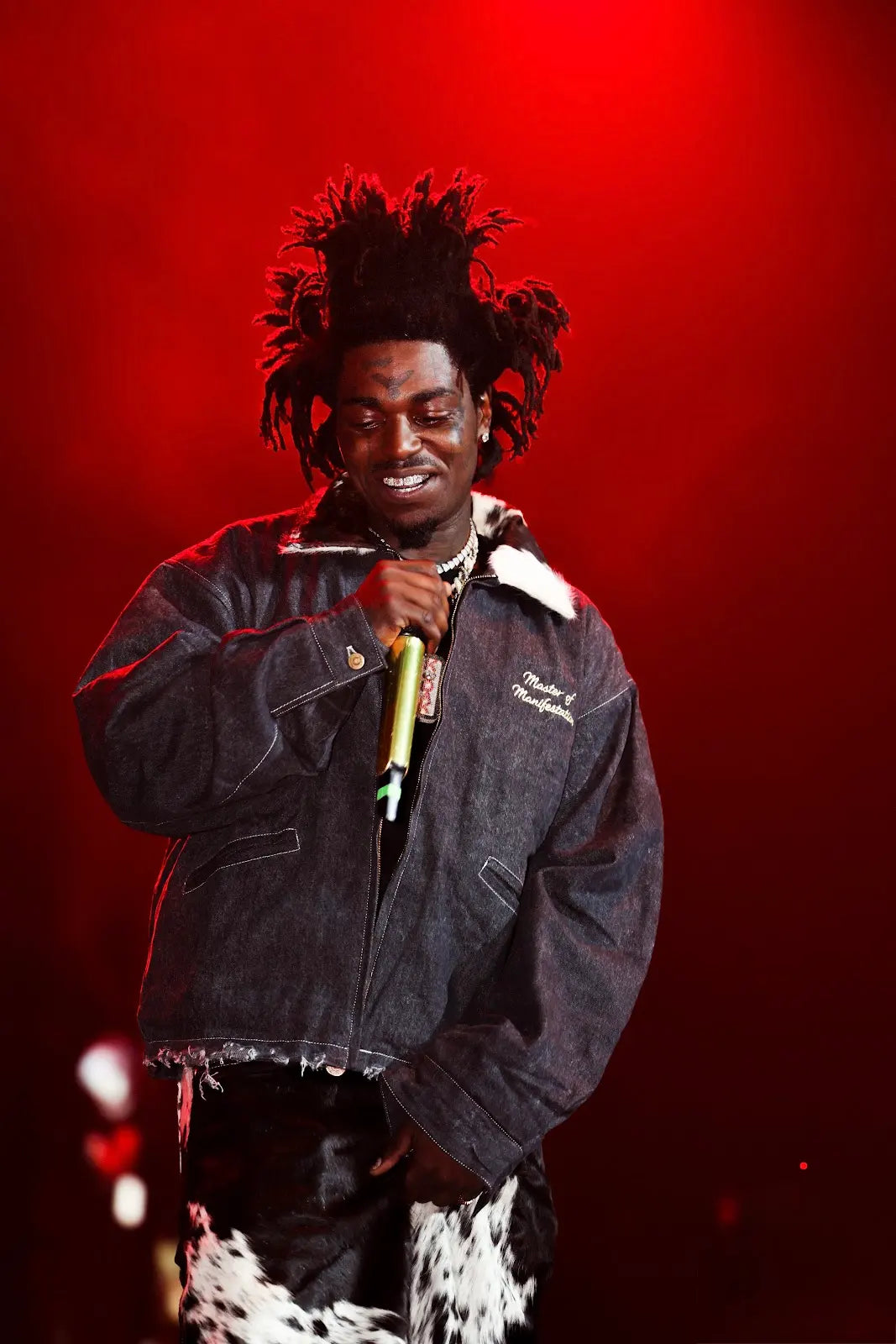 KODACK performing under red stage lights in a denim jacket with a cowhide collar and black-and-white cowhide jorts.